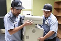 Two Fresno Unified staff employees lift and carry a printer.
